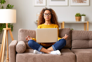 Young mixed race woman meditating with closed eyes while working or studying online in living room...