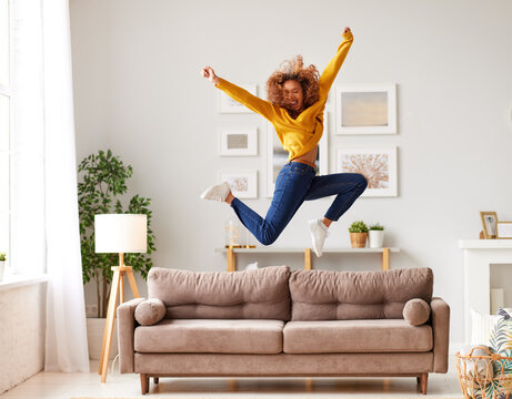 Happy african american teen girl jumping on sofa while having fun on weekend at home