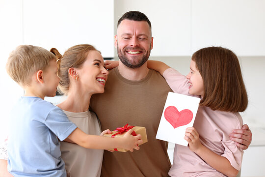 Mother and two smiling kids congratulating dad with Fathers day while standing in kitchen in morning