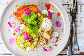 A serving of smashed avocado on toast with a poached egg and grilled tomato