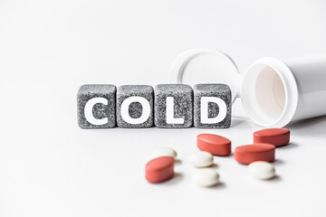 word COLD is made of stone cubes on a white background with pills. medical concept of treatment, prevention and side effects. small, shock-absorbing cushion found between bones vertebrae