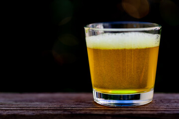 Glass of beer with a strong fizzy head and microscopic bubbles inside the beer glass displayed on a wooden table with a dark blurred background.