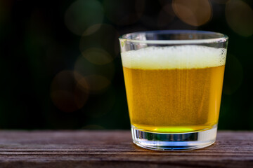 Glass of beer on wooden bench with blurry background.
