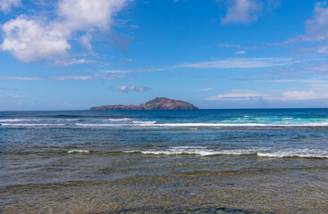 Landscape viewed from across the fringing reefs and turquoise coloured waters with shallow water on foreground .
