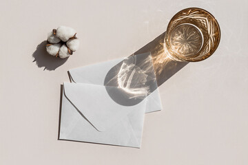 Still life scene with cotton flower on beige background in sunlight and envelope, invitation mockup.
