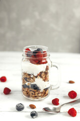 A jar of oatmeal granola with yogurt and fresh wild berries on a light background. Healthy breakfast or snack. Vertical photo. Copy space
