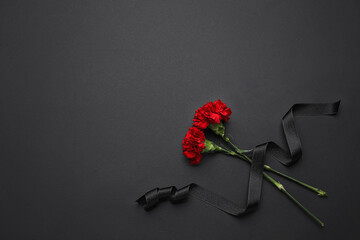 Black funeral ribbon with carnation flowers on dark background