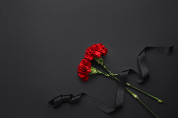 Black funeral ribbon with carnation flowers on dark background - obrazy, fototapety, plakaty