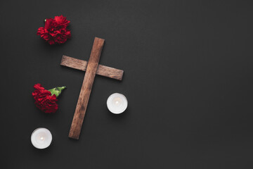Wooden cross with carnation flowers and candles on dark background