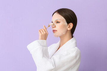 Beautiful young woman with sheet facial mask and massage tool on color background