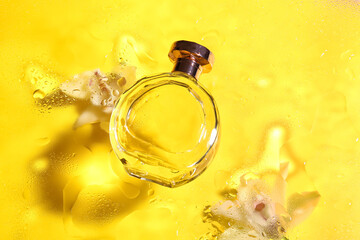 Bottle of perfume and flowers on glass with water drops