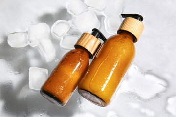 Bottles of cosmetic products and ice cubes on glass with water drops
