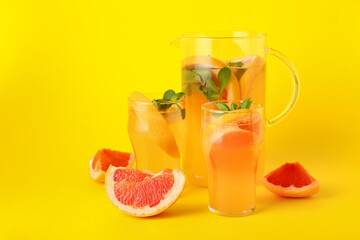 Glasses and jug of tasty grapefruit lemonade on color background