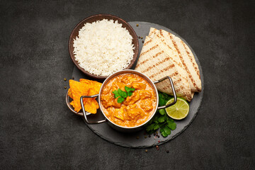 Pot of Traditional Chicken Curry, bowl of rice and pita on stone serving board