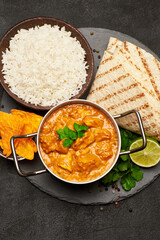 Pot of Traditional Chicken Curry, bowl of rice and pita on stone serving board