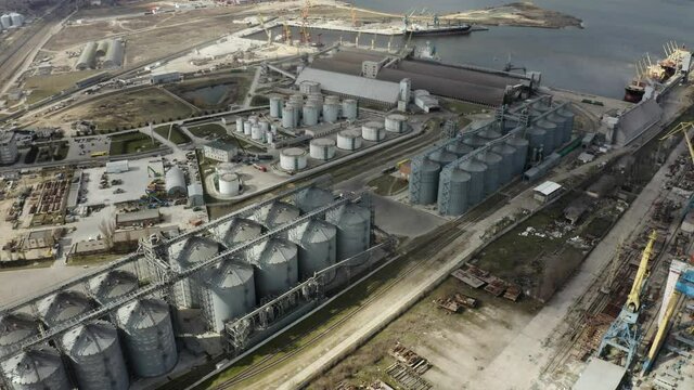 Grain elevator and silos near the river aerial view. Aerial view large waterfront grain storage facility with concrete silos and train yard. 