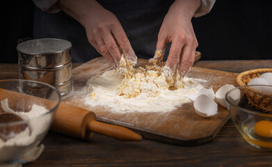 Women's hands, flour and dough. A woman in an apron prepares dough for homemade baking, a rustic home cozy atmosphere, a dark background with unusual lighting.