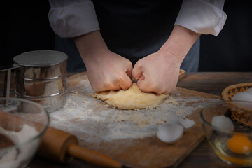 Women's hands, flour and dough. A woman in an apron cooking dough for homemade baking, a rustic home cozy atmosphere, a dark background with unusual lighting.