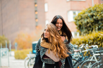 Two women having fun outside. Girl carrying friend on piggyback.