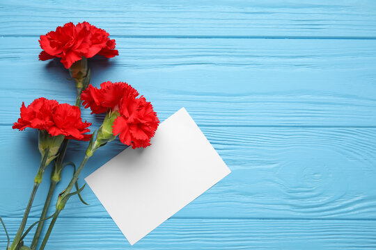Fresh carnation flowers with empty paper sheet on color wooden background