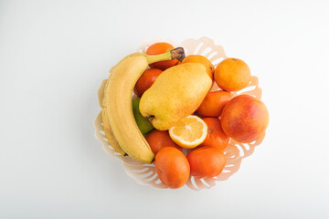 Fruit bowl top view on white background. Tangerines, banana, pear and other fruits in plate