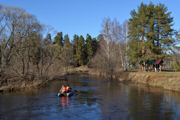 Kayaking on the river in the spring. A kayak with two athletes floats down the river on a sunny spring day, green trees, bright blue sky. People have picnics on the banks of the river.