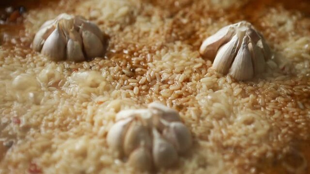 Garlic heads are stewed in rice with a bubbling sauce, steam comes. Aroma and seasoning for pilaf. Cooking pilaf in a cast-iron kazan, zirvak, oriental cuisine. Step 8 of 8