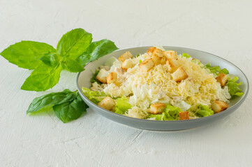 Traditional caesar salad in a plate on a white table with leaves, sauce, croutons and parmesan.