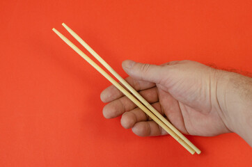 A man's hand holds wooden chopsticks against a red background.
