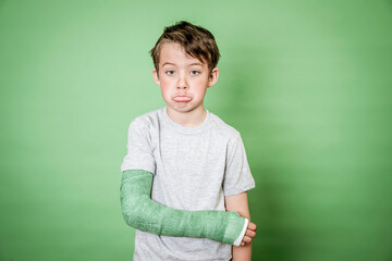 cool young schoolboy with broken arm and green plaster posing in front of green background in the studio