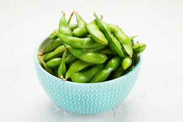 Raw edamame soya beans with salt and sauce on light gray background.