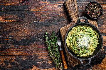 Spaghetti Pasta with pesto sauce, spinach and parmesan in a pan. Dark Wooden background. Top view. Copy space