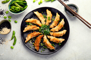 Fried gyoza dumplings with soy sauce and onion on light gray background.
