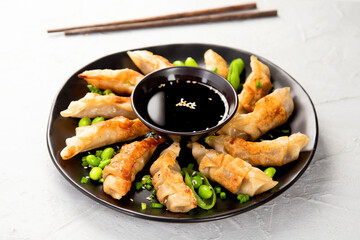 Fried gyoza dumplings with soy sauce and onion on light gray background.
