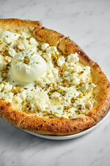 Pizza with cream cheese, buratta, cream sauce and pistachio on a white plate on a white marble background