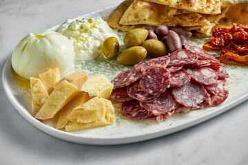 Italian antipasti snacks on white plate on marble background. Focaccia, burrata, olives, sun-dried tomatoes, salami, cheese, parmesan.