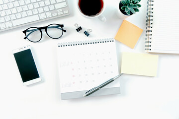 Modern white office desk table with computer, calendar, notebook, tree, glasses and cup of coffee. Top view with copy space,