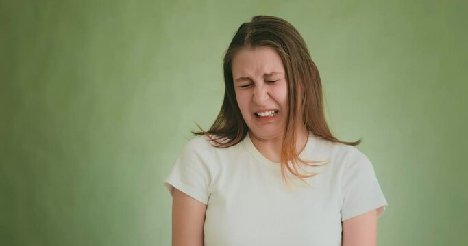 Pretty long haired disgusted woman in white t-shirt makes grimaces playing role on green background at audition slow motion