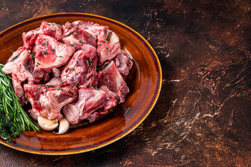 Raw mutton meat diced for goulash or stew with bone on a rustic plate. Dark background. Top view. Copy space