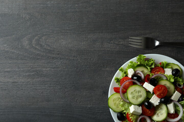 Plate of greek salad and fork on dark wooden background