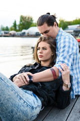Fototapeta premium Young sensual and loving couple sitting on a pier beside a river