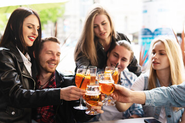 Friends celebrating and holding glasses with different alcohol drinks in a bar.
