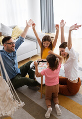 Happy young parents and children having fun, playing board game at home
