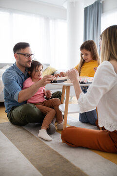 Happy Young Parents And Children Having Fun, Playing Board Game At Home