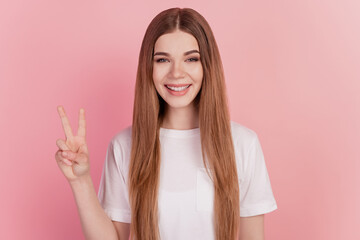 Happy smiling young cute woman showing two fingers victory gesture on pink wall