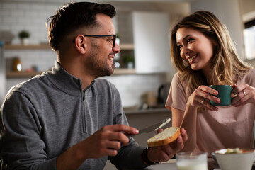 Happy girl enjoying in breakfast with her boyfriend. Loving young couple drinking coffee and eating sandwich at home...