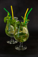 Summer mint lime refreshing cocktail mojito with rum and ice in glass on black background. Mojito cocktail on dark stone table. Glassy high glass for drinks. Lemonade at the bar.