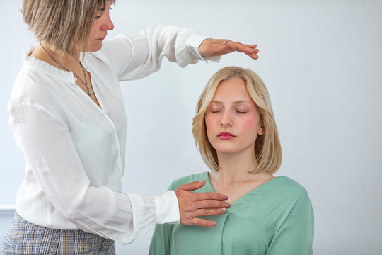 Professional Reiki healer doing Reiki treatment to young woman in health spa center. Healing and balancing heart and crown chakras. Attractive young woman having reiki treatment