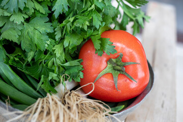 On the natural wooden table, there are vegetables such as spring onion tomatoes and parsley for authentic copper plate.