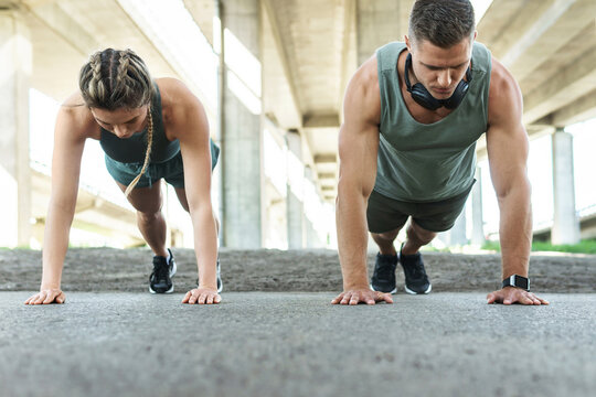 Athletic couple and fitness training outdoors. Man and woman doing push-ups exercise. - Powered by Adobe